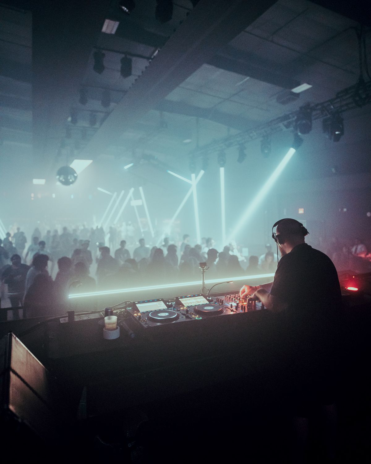 OldGold at the decks, seen from behind, playing to a full room under cyan light
